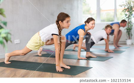 Pleasant preteen girl practicing variation of warrior pose of yoga with her family Pleasant preteen girl practicing variation of warrior pose of yoga with her family 102153534