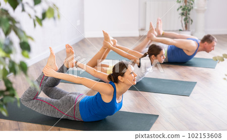 Happy middle-aged woman practicing bow pose of yoga with her family 102153608
