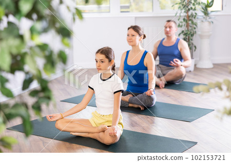 Pleasant preteen girl practicing lotus pose of yoga with her family Pleasant preteen girl practicing lotus pose of yoga with her family 102153721