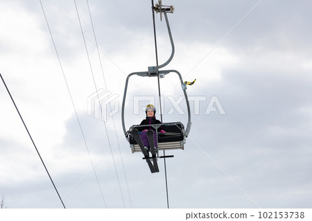 Woman in ski outfit raising on chairlift to slopes for skiing Woman in ski outfit raising on chairlift to slopes for skiing 102153738