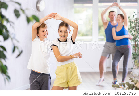 Happy preteen boy and girl practicing dance in pairs together with their parents 102153789