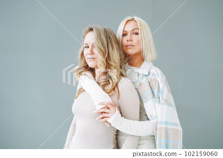 Portrait of young blonde women friends in sportswear on background of grey wall Portrait of young blonde women friends in sportswear on background of grey wall 102159060