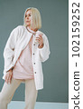 Portrait of young blonde woman in sportswear with thermocup on background of grey wall 102159252