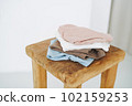 Stack of cotton tops in natural tones on wooden chair in bright room 102159253