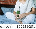 Crop photo of Young woman in casual clothes with green smoothie sitting on bed at the home 102159261