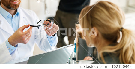 Close up of ophthalmologist helps the client to choose a more suitable spectacle frame Close up of ophthalmologist helps the client to choose a more suitable spectacle frame 102160443