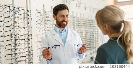 Male optician showing glasses to woman at optics store 102160444
