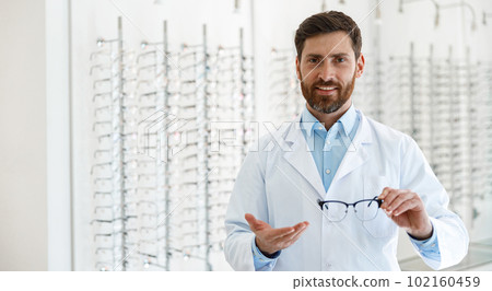 Portrait of ophthalmologist offering glasses to client in optics store 102160459