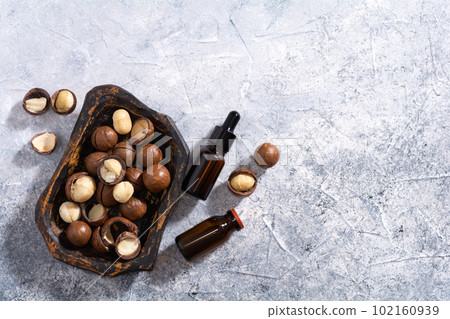 Natural macadamia nut oil in a bottle. Cosmetic oil. Top view macadamia nuts in old wooden plate on a gray background. 102160939