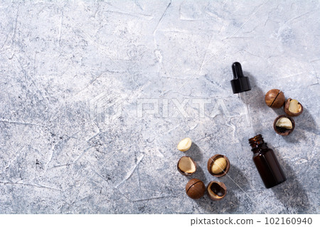 Natural macadamia nut oil in a bottle. Cosmetic oil. Top view macadamia nuts on a gray background. Natural macadamia nut oil in a bottle. Cosmetic oil. Top view macadamia nuts on a gray background. 102160940