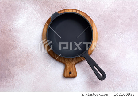 Cast iron skillet on a wooden cutting board on light background. Kitchen utensils. Empty place. Top view. Cast iron skillet on a wooden cutting board on light background. Kitchen utensils. Empty place. Top view. 102160953