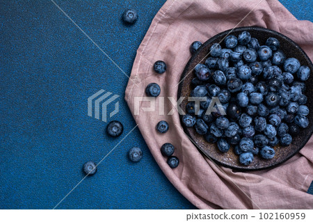 Plate with fresh blueberries on a blue background. Napkin with fresh berries. View from above. Focus on the plate Plate with fresh blueberries on a blue background. Napkin with fresh berries. View from above. Focus on the plate 102160959