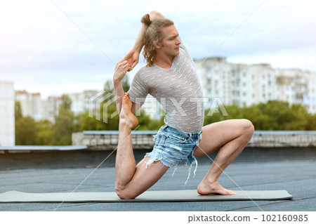 A man practices yoga on the roof of the house. Yoga at sunset. Healthy life, sport and meditation concept. A man practices yoga on the roof of the house. Yoga at sunset. Healthy life, sport and meditation concept. 102160985