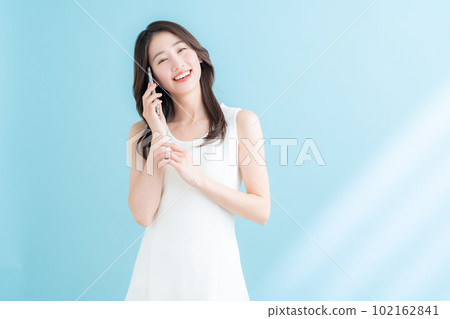 A young woman operating a smartphone on a blue background where the sun shines A young woman operating a smartphone on a blue background where the sun shines 102162841