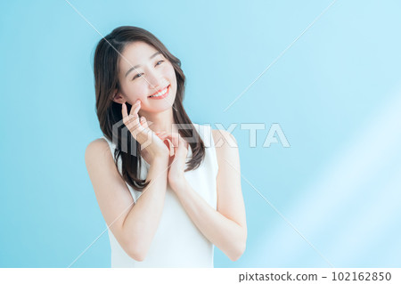 一位在陽光普照的藍色背景下做護膚的年輕女性 102162850