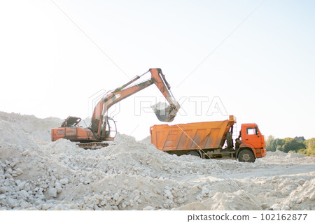 The excavator collects stones in a bucket and puts them in a truck. Working machines at road construction 102162877