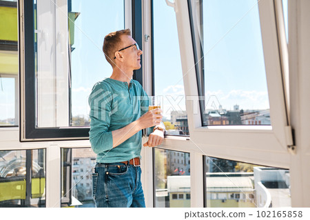 Middle aged man stands on balcony of high-rise building 102165858