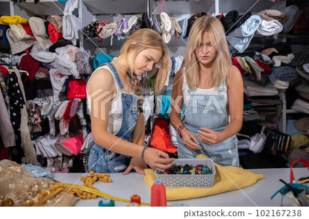 A designer and a student look for buttons for a selected fabric in a tailor's shop. 102167238