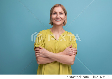 smiling blond mature woman in yellow tank top posing confidently on blue background 102169302