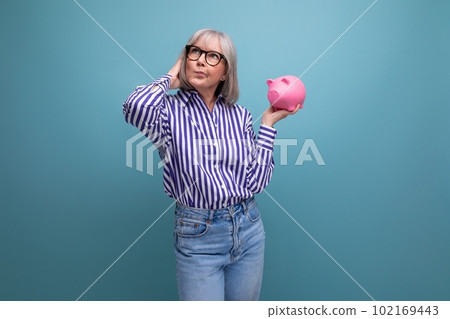 smart 60s woman with gray hair holding piggy bank on bright studio background 102169443