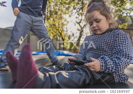 children sit on a trampoline and look at the phone 102169597