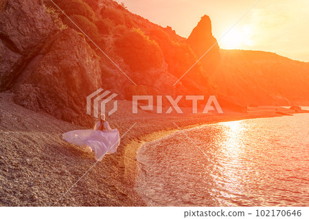 Mysterious woman silhouette long hair walks on the beach ocean water, sea nymph wind listens to the wave. Throws up a long white dress, a divine sunset. Artistic photo from the back without a face Mysterious woman silhouette long hair walks on the beach ocean water, sea nymph wind listens to the wave. Throws up a long white dress, a divine sunset. Artistic photo from the back without a face 102170646