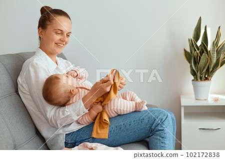 Horizontal shot of attractive young adult mother sitting on sofa with her toddler daughter, expressing happiness, smiling happily, motherhood and childhood. Horizontal shot of attractive young adult mother sitting on sofa with her toddler daughter, expressing happiness, smiling happily, motherhood and childhood. 102172838