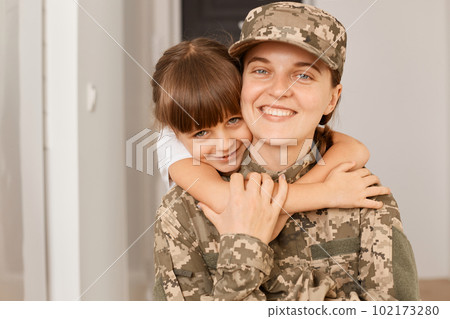 Portrait of female with toothy smile posing with her daughter after returning from army or exercising, kid embracing her mommy, missing her little girl. 102173280