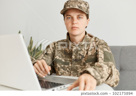 young adult female soldier wearing military costume, posing indoor in light room and looking at camera with serious facial expression, being unhappy and tired. young adult female soldier wearing military costume, posing indoor in light room and looking at camera with serious facial expression, being unhappy and tired. 102173894