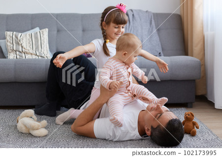 Happy family enjoying weekend together, lying on floor and having fun, people wearing casual style clothing, posing in living room near sofa, happy childhood and parethood. 102173995