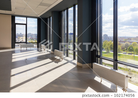 A large, spacious, empty room with huge windows and floor-mounted central heating radiators with temperature controllers. 102174056