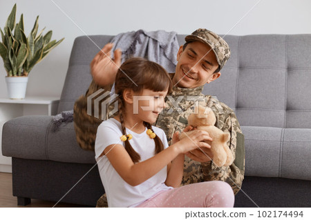 Image of positive optimistic young adult soldier man wearing camouflage uniform returning home after army, spending time with daughter, dad being glad to see his child after long time separation. Image of positive optimistic young adult soldier man wearing camouflage uniform returning home after army, spending time with daughter, dad being glad to see his child after long time separation. 102174494