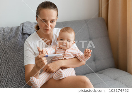 Astinished Caucasian beautiful woman wearing wnhite t shirt got shocked when pregnancy test showing positive result, young mother holding toddler baby girl in hands while sitting on sofa at home. Astinished Caucasian beautiful woman wearing wnhite t shirt got shocked when pregnancy test showing positive result, young mother holding toddler baby girl in hands while sitting on sofa at home. 102174762