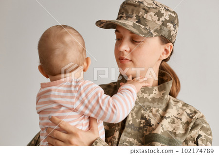 Portrait of emotional military mother, dressed in camouflage, holding her young daughter in arms, greeting after returning home from a tour of duty overseas. 102174789