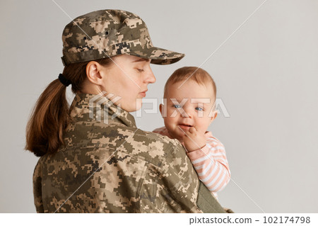 Caucasian military mother wearing camouflage uniform and hat, posing with her infant baby, haven't seen her daughter long time, missing her kid while served in army. 102174798