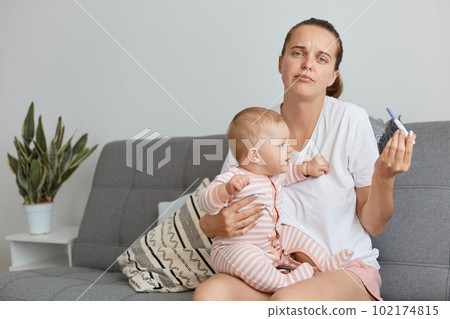 Confused female wearing white casual style t shirt posing with her infant daughter and pregnancy test in hands, shrugging her shoulders, doesn't know what to do now. Confused female wearing white casual style t shirt posing with her infant daughter and pregnancy test in hands, shrugging her shoulders, doesn't know what to do now. 102174815