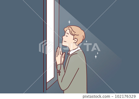 Religious man prays standing at window and holds chain with catholic christian crucifix in hands Religious man prays standing at window and holds chain with catholic christian crucifix in hands 102176329