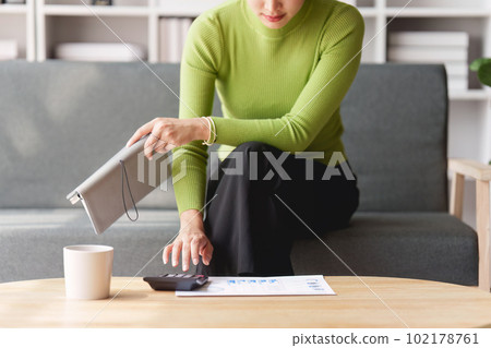 Woman sits on sofa at home, studying and analyze house bills and submitting tax forms. Woman sits on sofa at home, studying and analyze house bills and submitting tax forms. 102178761