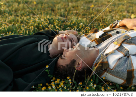 Side view of relaxed young couple lying together on green grass with eyes closed. Relationships concept Side view of relaxed young couple lying together on green grass with eyes closed. Relationships concept 102178768
