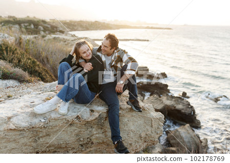 Portrait of a middle-aged couple sitting on a rock at the beach in Cyprus. They are wearing casual clothes 102178769