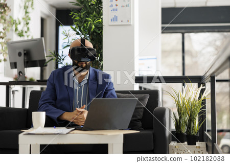 Arab business worker analyzing financial data in metaverse using vr glasses in start up office. Young man professional brainstorming wearing virtual reality headset in green open space Arab business worker analyzing financial data in metaverse using vr glasses in start up office. Young man professional brainstorming wearing virtual reality headset in green open space 102182088