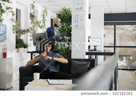 Happy businessman recording business ideas using smartwatch app while sitting on couch in office. Smiling arab executive manager talking on electronic wearable watch device Happy businessman recording business ideas using smartwatch app while sitting on couch in office. Smiling arab executive manager talking on electronic wearable watch device 102182261