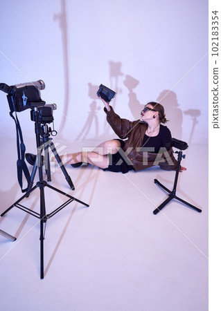 Stylish young girl in leather jacket, dress and trendy sunglasses posing with retro video cameras, filming, making content Stylish young girl in leather jacket, dress and trendy sunglasses posing with retro video cameras, filming, making content 102183354
