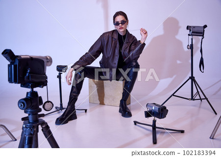 Brutal look. Beautiful young girl in stylish, trendy clothes, leather jacket, pants, sunglasses and accessories. Retro cameras in studio Brutal look. Beautiful young girl in stylish, trendy clothes, leather jacket, pants, sunglasses and accessories. Retro cameras in studio 102183394