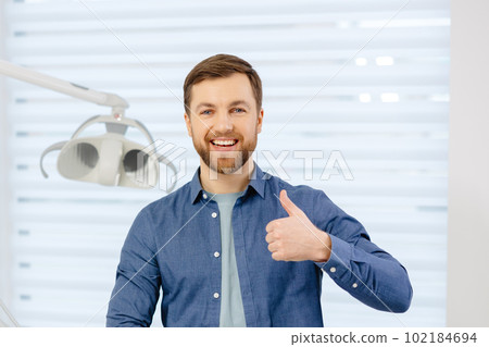 Portrait of happy patient near dental chair and shows a gesture with a thumb up class, good. Modern dentistry with the use of new technologies 102184694