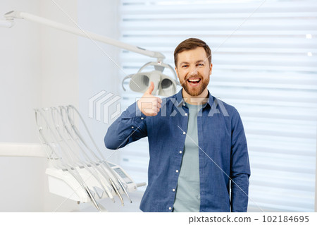 Portrait of happy patient near dental chair and shows a gesture with a thumb up class, good. Modern dentistry with the use of new technologies 102184695