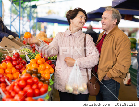Aged man and woman customers buying vegetables in open-air market Aged man and woman customers buying vegetables in open-air market 102185121