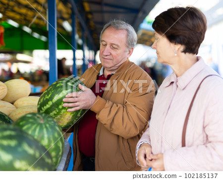 Cheerful elderly casual male and female picking fresh organic watermelon at local market 102185137