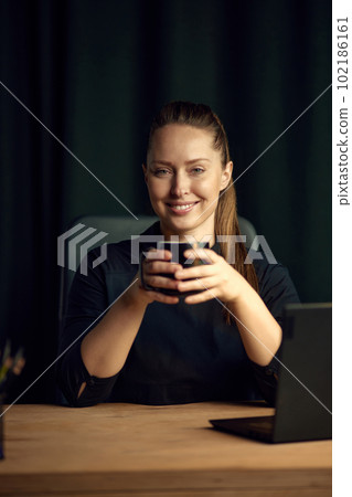 Portrait of beautiful, confident, smiling, young businesswoman sitting at table with cup, posing, looking at camera 102186161