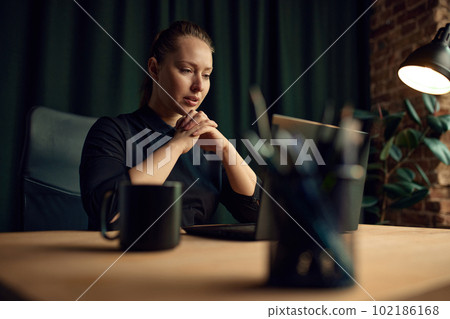 Concentrated, attentive, serious business woman, professional, boss, sitting at table in her office, looking on laptop and working Concentrated, attentive, serious business woman, professional, boss, sitting at table in her office, looking on laptop and working 102186168